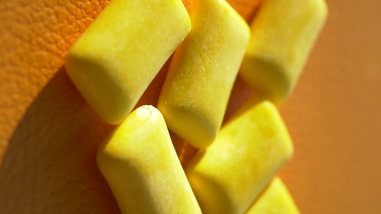 Close-up of yellow chewing gum pieces on an orange surface
