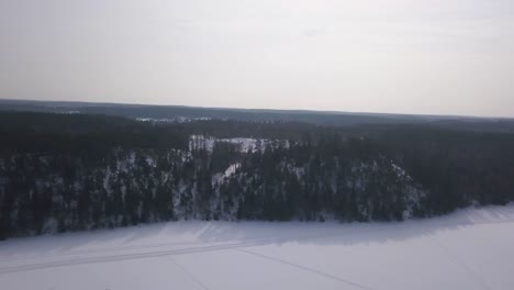 Smooth-slow-panning-aerial-shot-of-frozen-lake-in-foreground-with-huge-evergreen-forest-in-the-background
