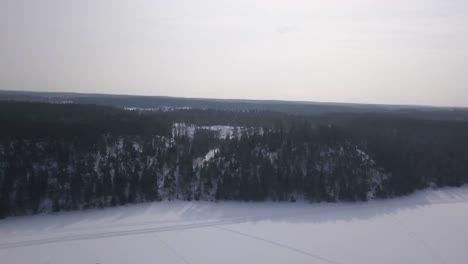 smooth slow panning aerial shot of frozen lake in foreground with huge evergreen forest in the background