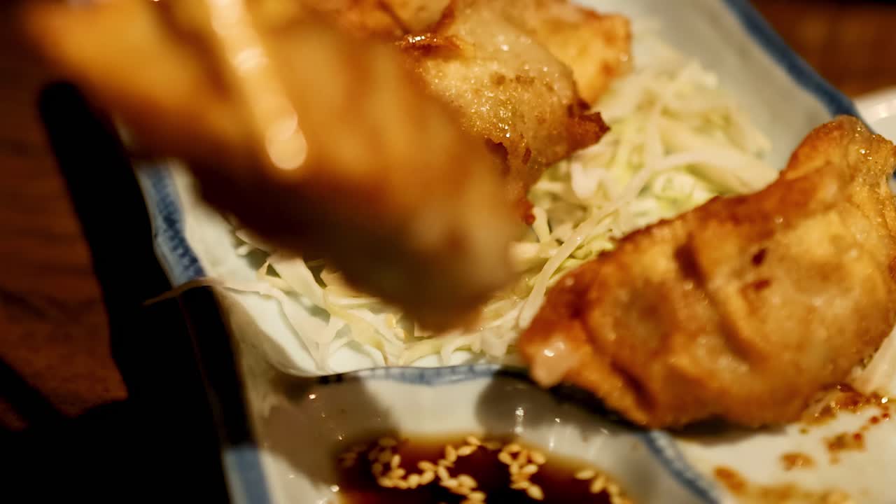Close-up of chopsticks picking crispy gyoza from a plate with cabbage and soy sauce.