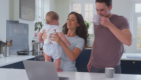 Amorosa-Familia-Transgénero-Con-Un-Bebé-En-Casa-Junto-Con-Una-Computadora-Portátil-Tomando-Café-En-El-Mostrador-De-La-Cocina