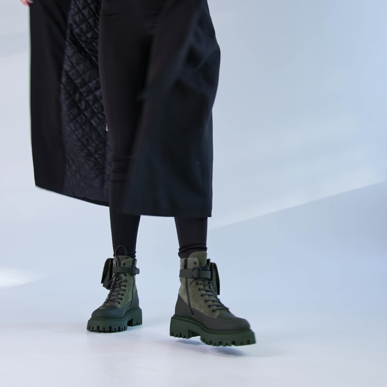 Girl in black coat presenting her fashionable modern boots on tractor soles. Studio footwear demonstration