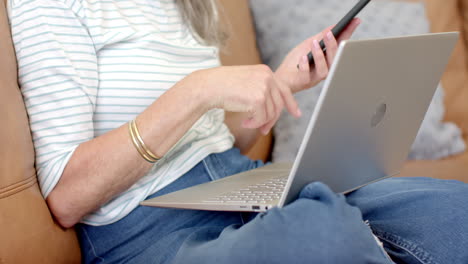 mujer caucásica de cabello gris usando teléfono inteligente y portátil