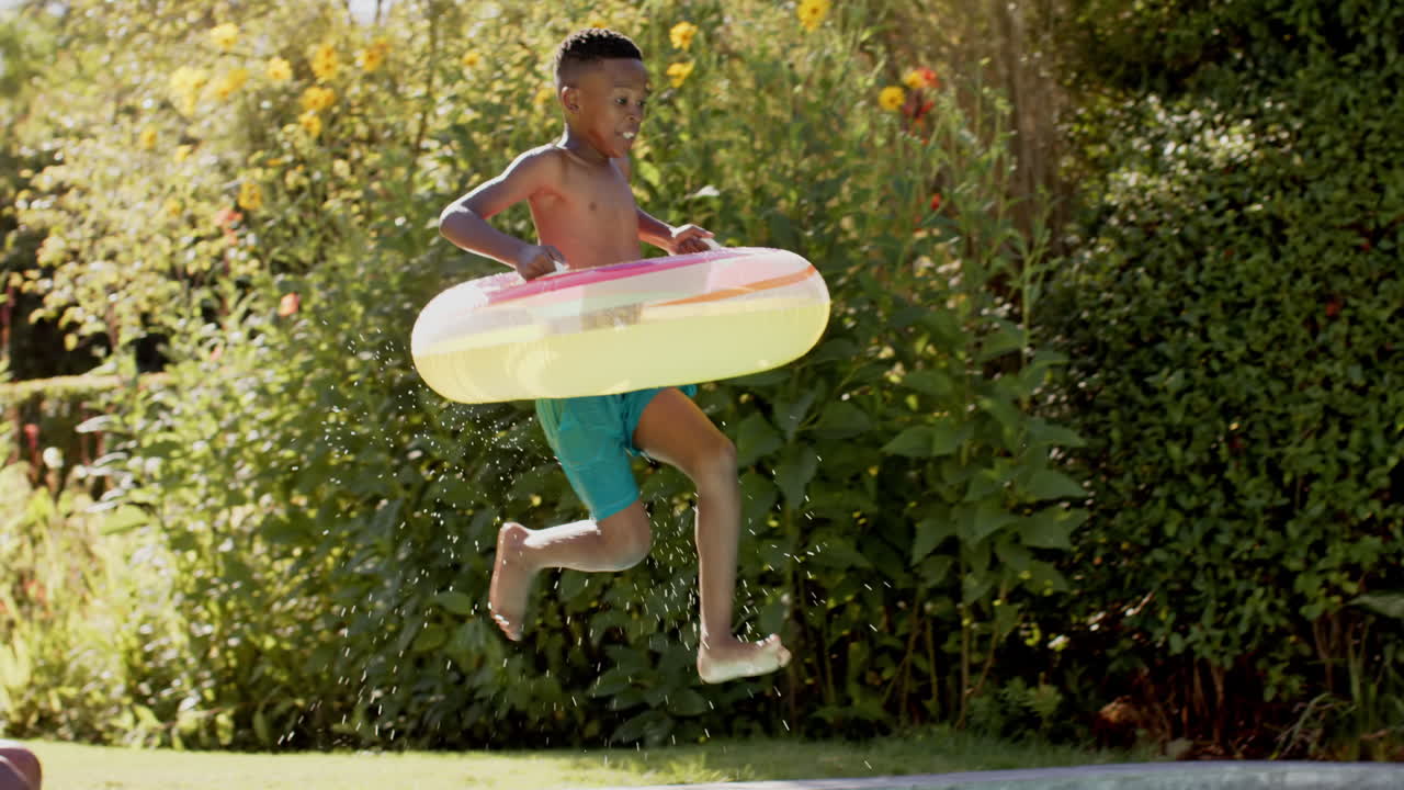 Enjoying summer, young boy jumping into pool with family