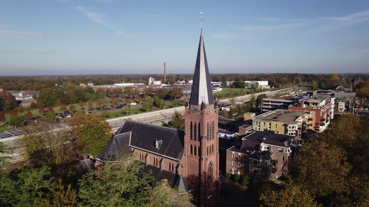 Parish St. Antonius of Padua church in Dutch town Nijverdal seen from above on a sunny day with the tower rising above countryside landscape and train station tunnel in the background