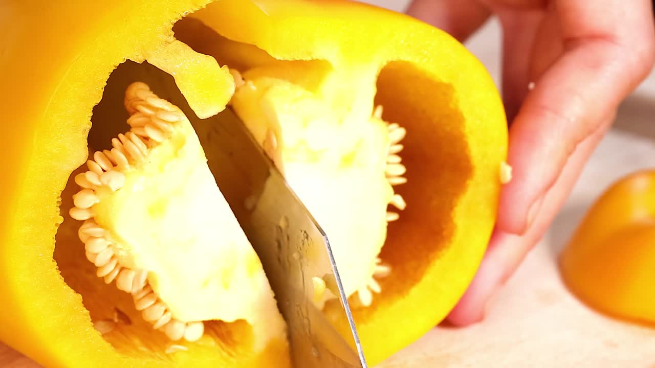 A knife carefully slices through a yellow bell pepper, focusing on the seeds and inner core.