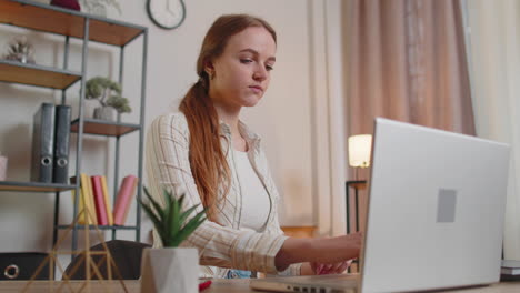 Young-woman-girl-using-laptop-computer-sitting-at-table-working,-typing-on-keyboard-from-home-office