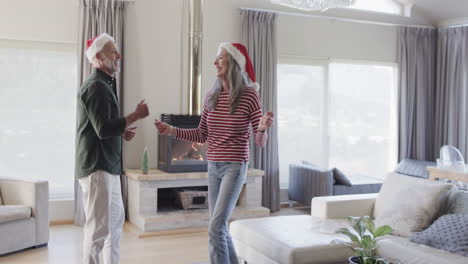 middle aged caucasian couple in santa hats dancing at christmas at home, slow motion