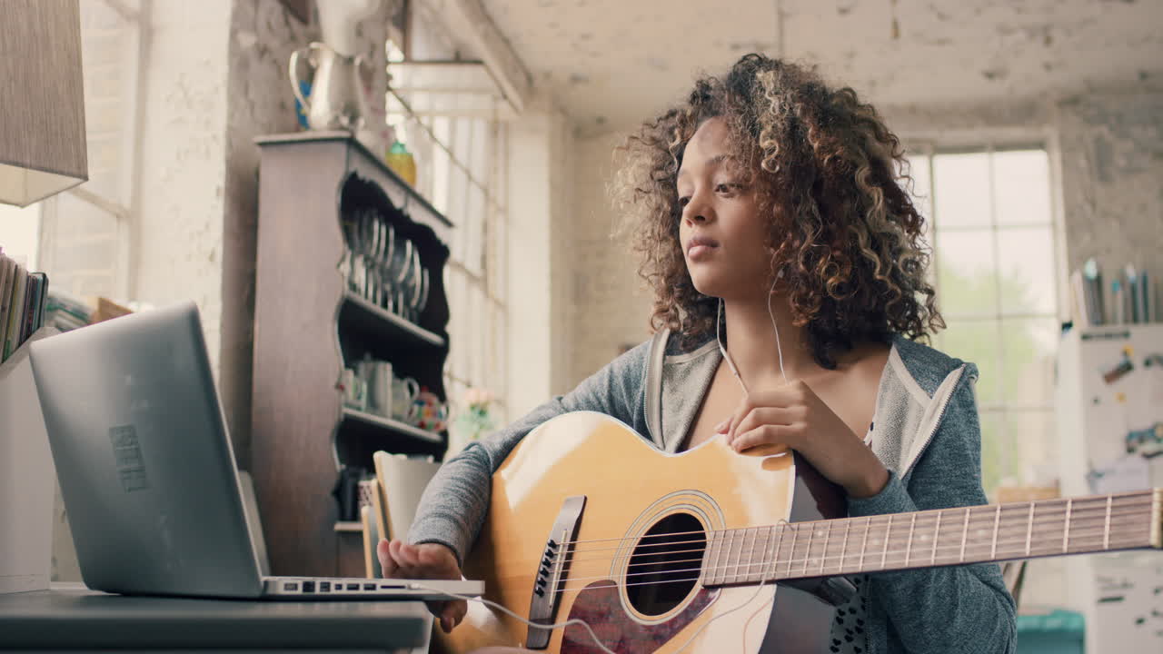 chica joven de raza mixta atractiva aprendiendo a tocar la guitarra usando una computadora portátil