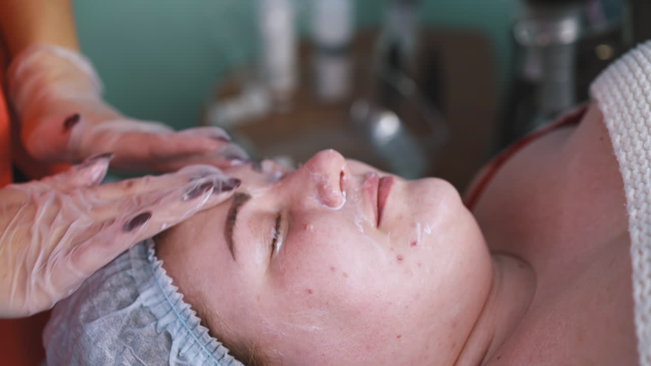 Kosmetolog påfører creme og masserer ansigtet på en kvinde med fyldigere figur