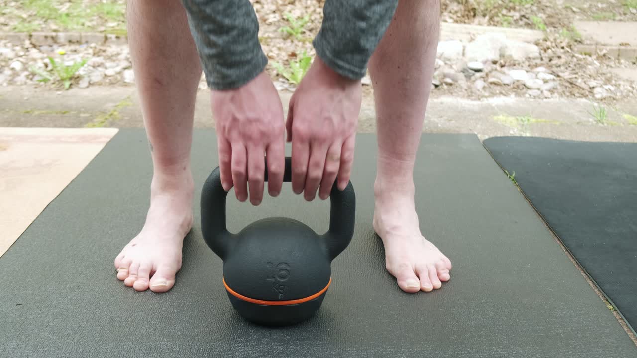 Close up of a man doing a deadlift with a 16 kg kettlebell outside in slow motion 4K