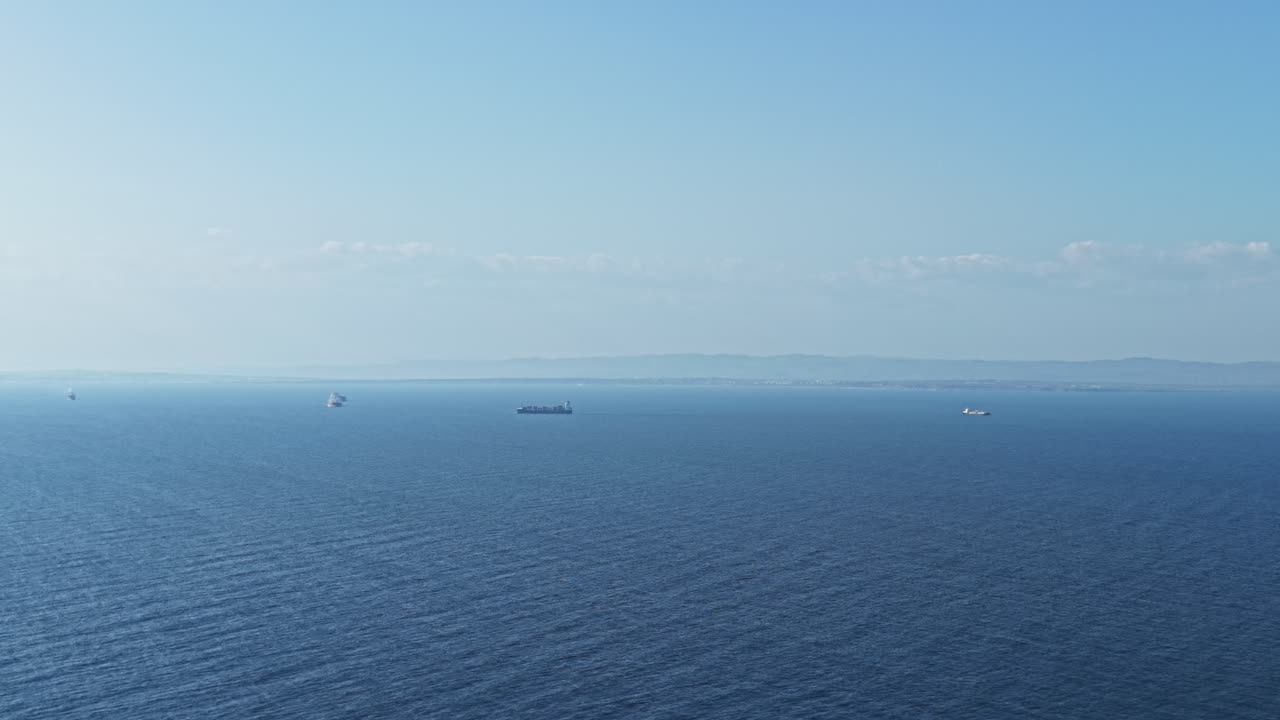 Ships sail across the horizon on a clear day with calm waters