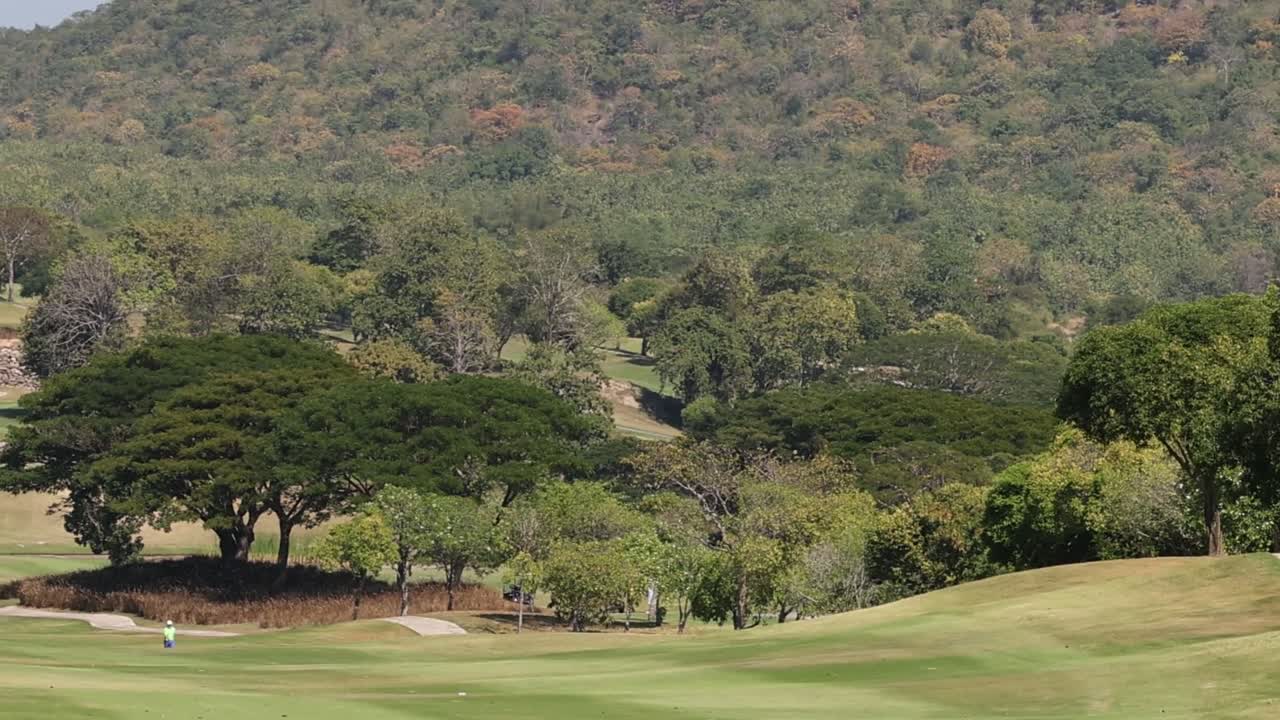 A serene view of a golf fairway surrounded by trees and hills under a clear sky.