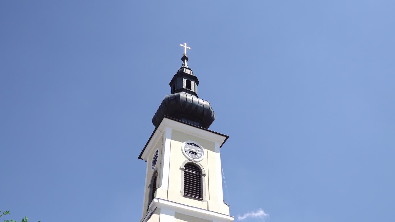 Lenta ripresa aerea del campanile di una chiesa chiara, cielo blu e un uccello che attraversa l'inquadratura