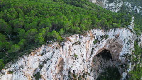 Hikers-rest-on-a-rocky-cliff-among-trees-with-a-view-of-the-green-landscape-during-sunset-in-ibiza