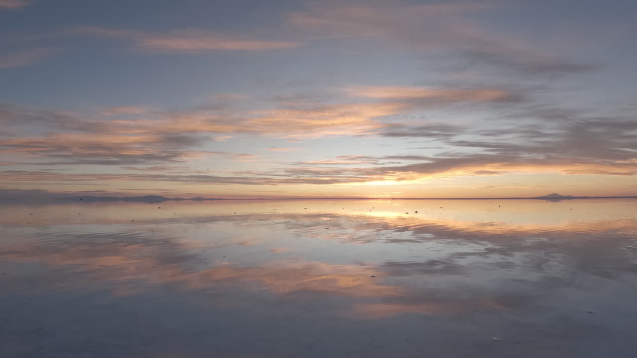 timelapse durante la puesta de sol en las llanuras de sal de bolivia américa del sur con el cielo rosado y naranja reflejado en el agua del espejo en un día soleado con nubes y sin gente y una montaña en el fondo