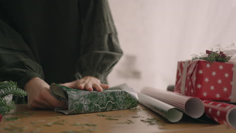 a close-up of the hand of a woman wraps her hands around a box in a wrapping paper with a christmas ornament. professional decorator gift wrapper