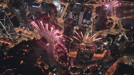 circling aerial drone shot of exploding fireworks on top of high-rise buildings in hong kong at night