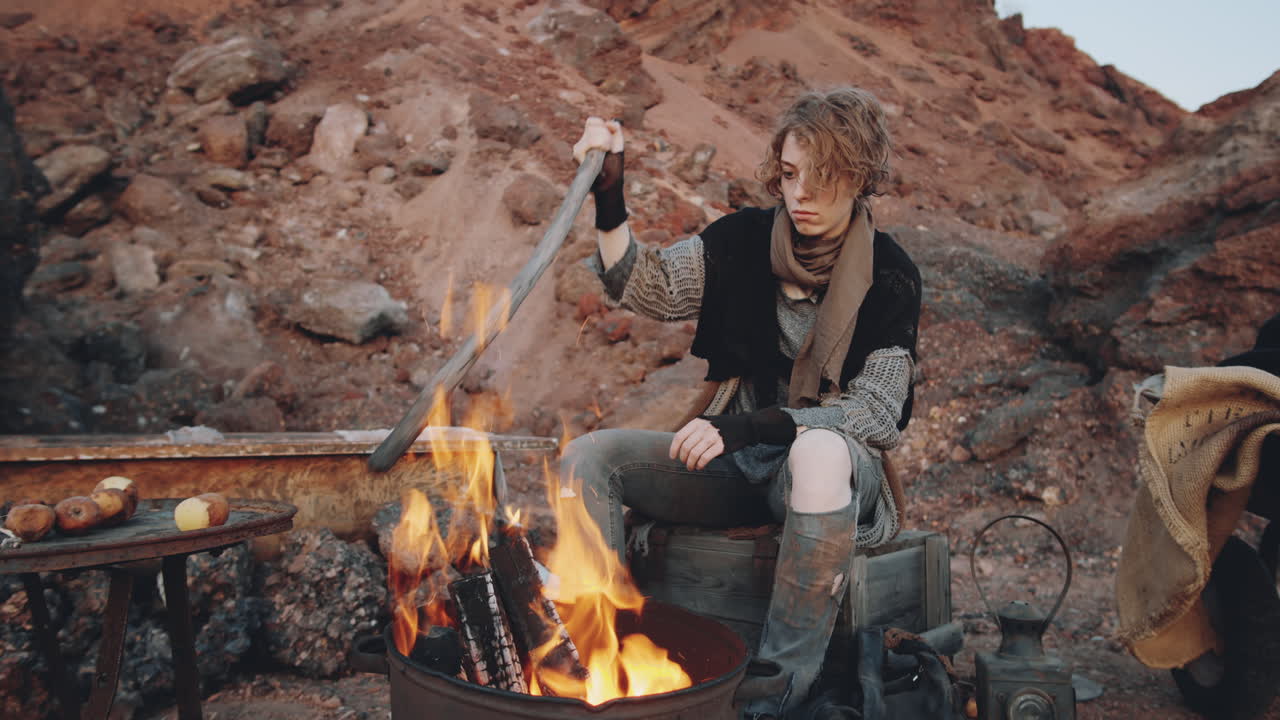 Dystopian Woman Sitting by Campfire in Garbage Can