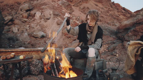 Dystopian-Woman-Sitting-by-Campfire-in-Garbage-Can