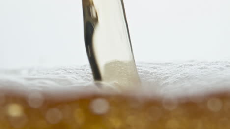 closeup beer stream pouring on bubbling drink surface at white background.