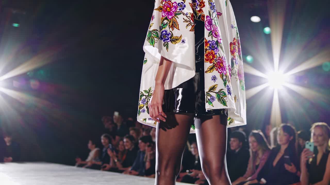 Videooptagelse i lav engel af en model på en catwalk, der viser en blomstret kappe