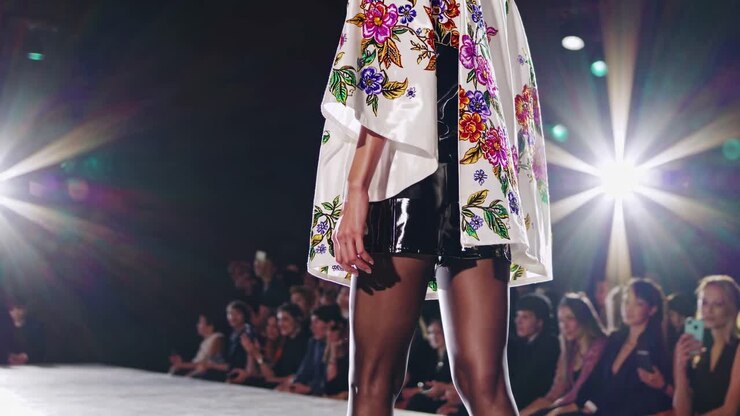 Videooptagelse i lav engel af en model på en catwalk, der viser en blomstret kappe