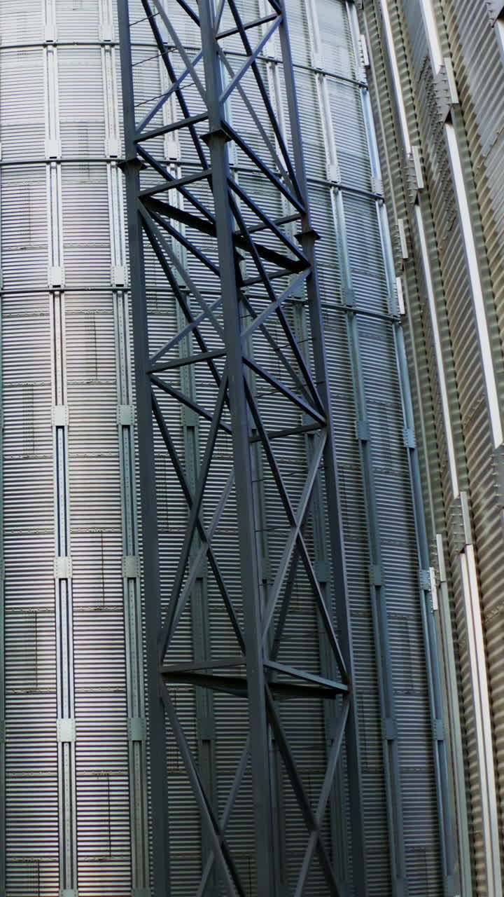 Exterior of modern plant. Large metal grain elevators outdoors. Aluminum containers for storing and processing crop. Close-up.Camera rising up. Vertical video