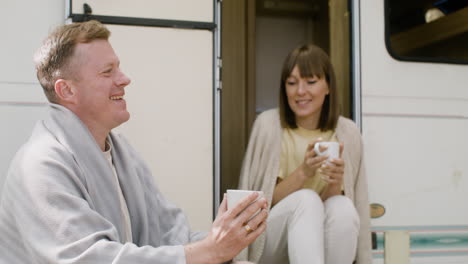 happy couple talking and drinking hot coffee at the camping in the forest