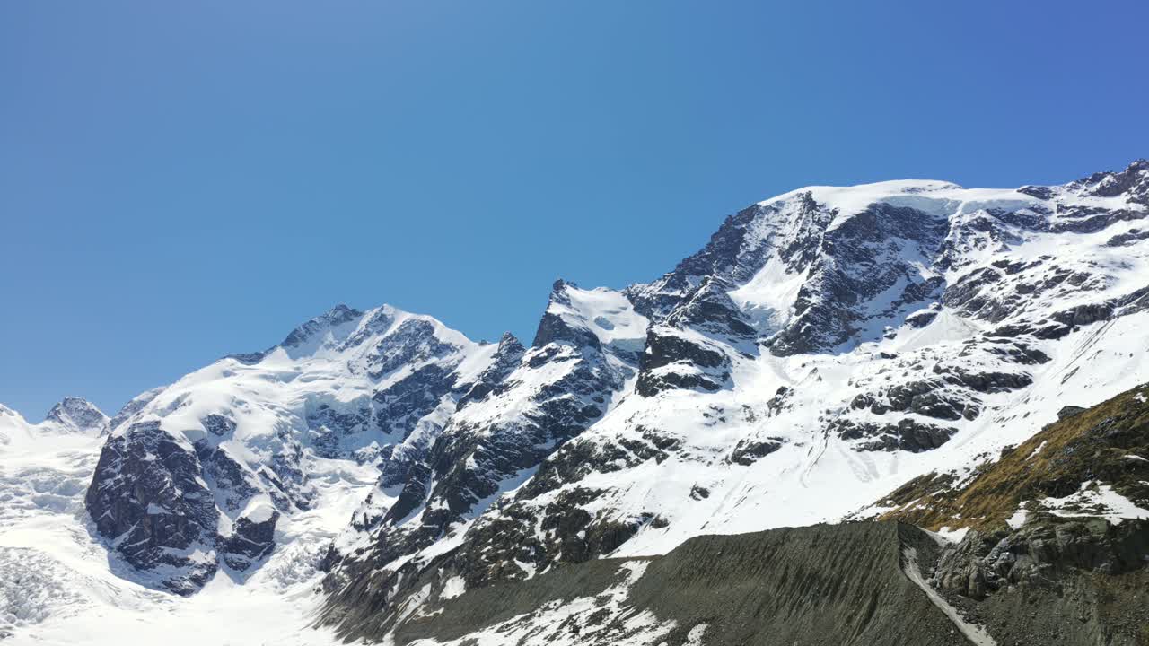 Snow-covered peaks and glaciers of Morteratsch massif in Swiss Alps under clear blue sky. Aerial drone low-angle pov, copy space