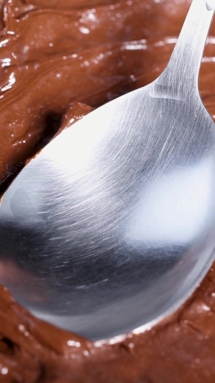 Primo piano di un cucchiaio che mescola una miscela liscia di cioccolato fuso