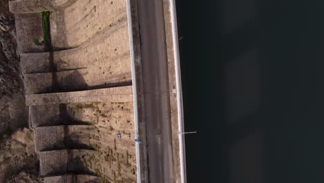 top down aerial view of dam, drone flying above road, between water and wall