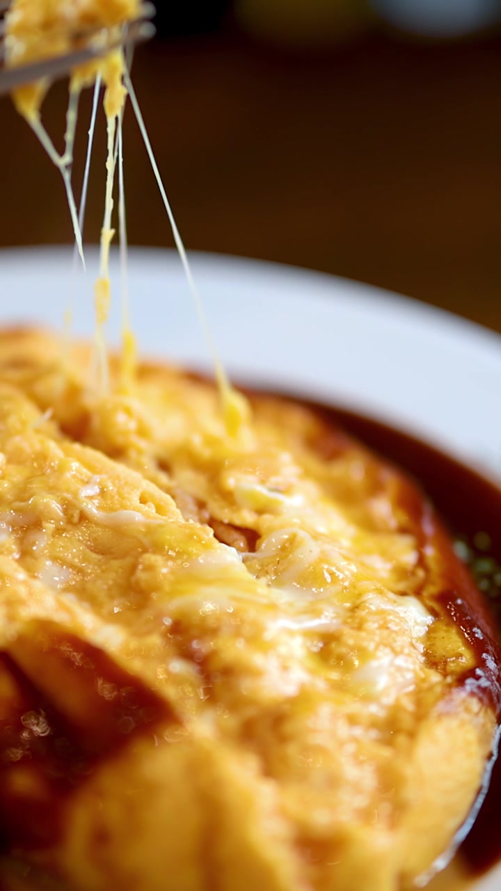 Detail vidličky zvedající sýrové omurice s demi-glace omáčkou v teplém osvětlení restaurace.