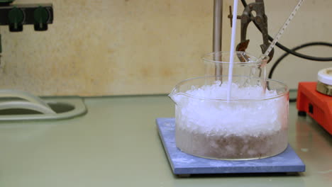 chemical solution in a beaker with thermometer, cooling with ice for an experiment - close up, slow motion