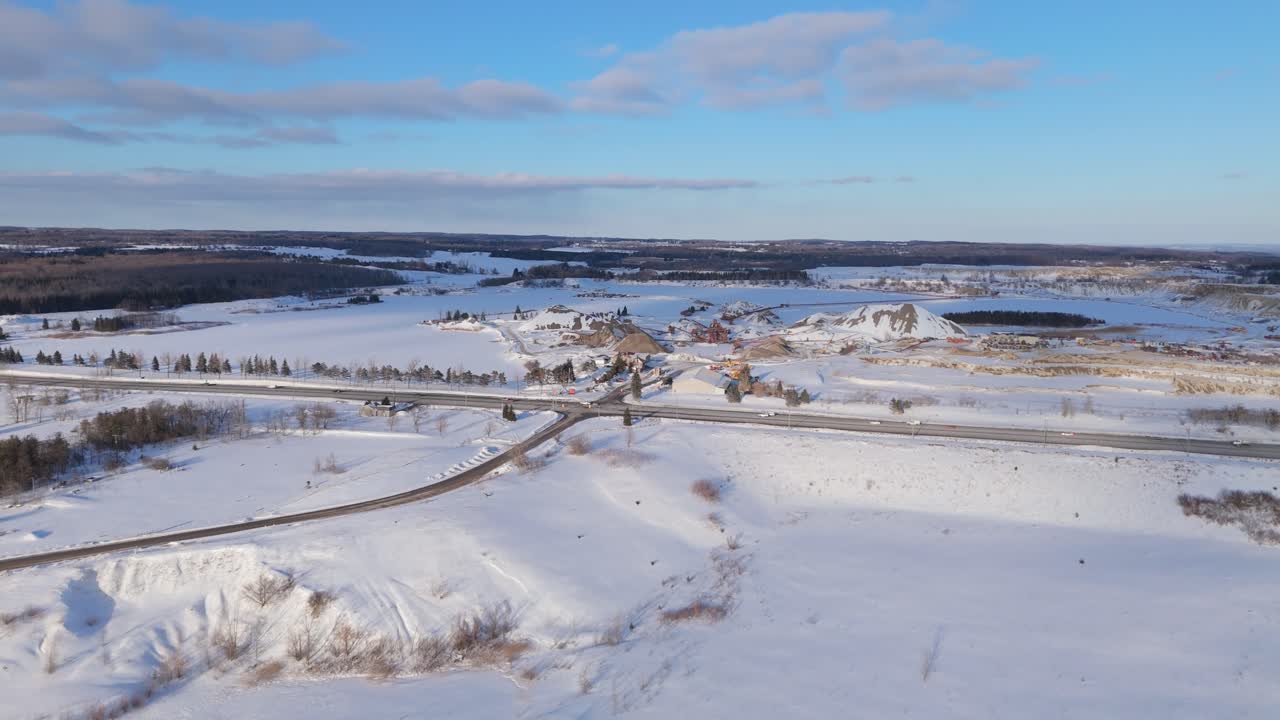 Winterse luchtbeelden tonen een zandgroeve en Highway 10 die door een besneeuwd landschap loopt in Caledon Village, Ontario. Auto's bewegen door het tafereel onder een zonnige winterhemel