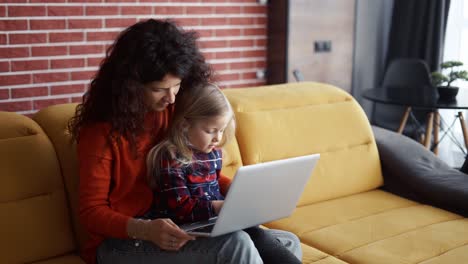 madre e hija sentadas en el sofá y usando una computadora portátil