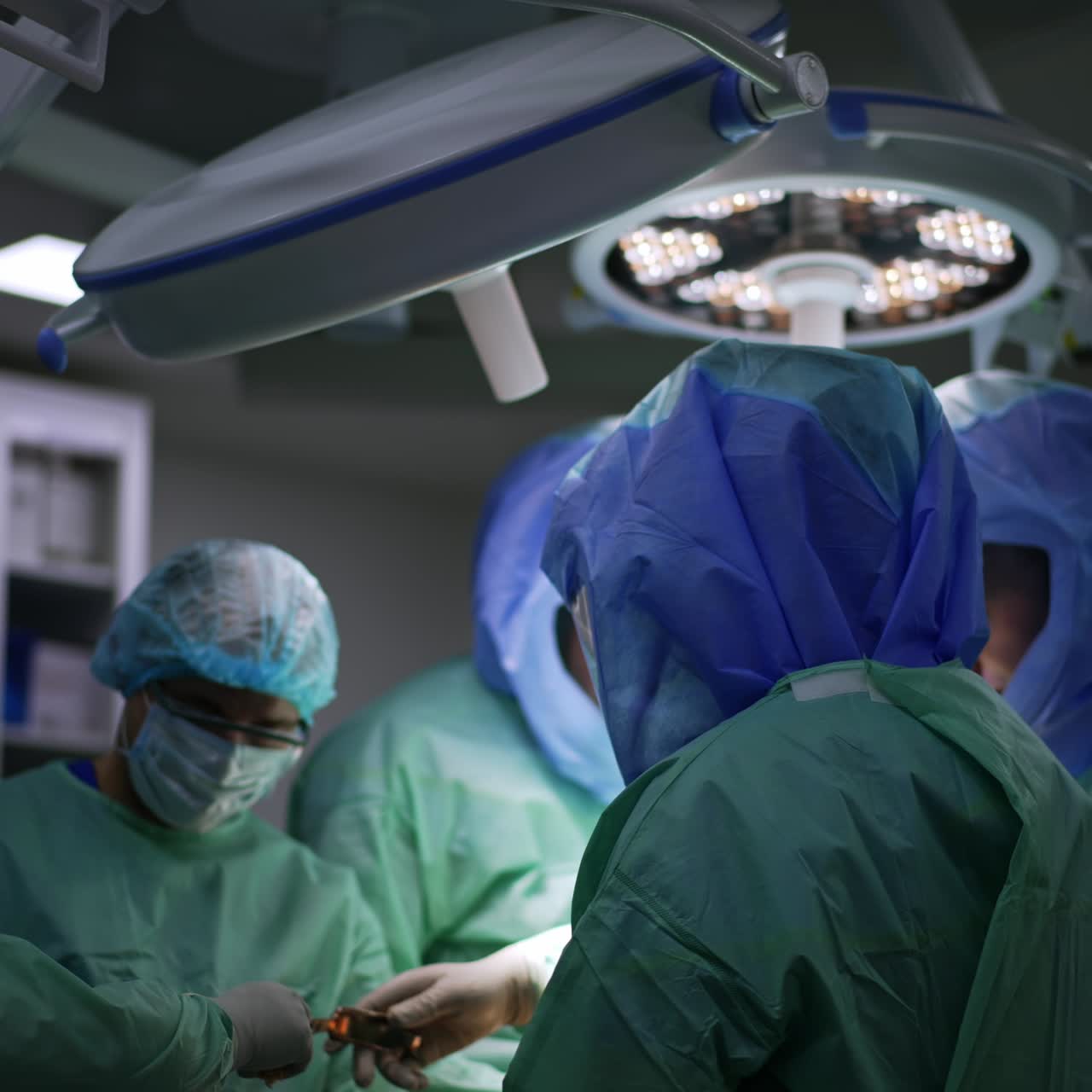 Male surgeons wearing protective suits and helmets work in modern operational room. Professionals perform arthroscopic procedure