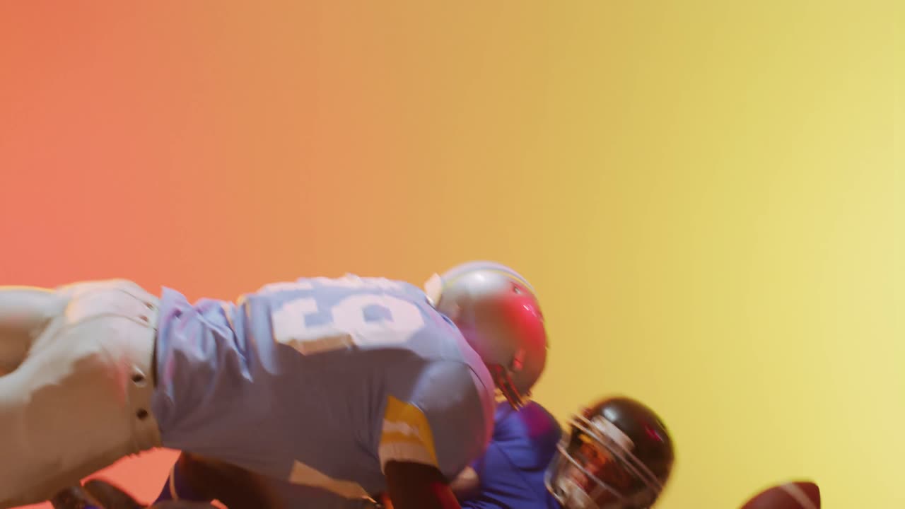 Video pemain football Amerika beragam etnis sedang melakukan tackle dengan bola di latar belakang kuning ke oranye.