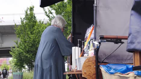 an elderly woman buys coffee at an outdoor stall on a summer day