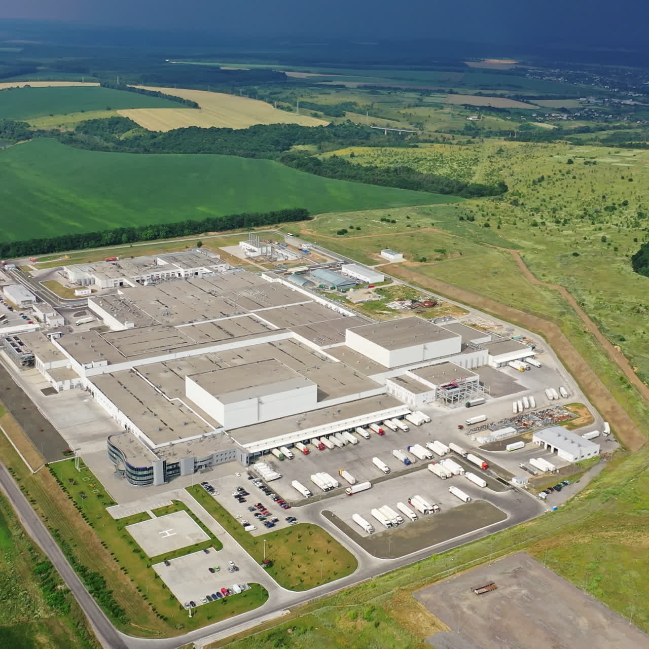 Aerial view on a modern manufacturing complex in summer. Top view of an industrial plant among green fields and forests. Camera is rising up.