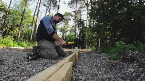 carpenter hitting wood stakes into ground with a sledge hammer. formwork for concrete pad.