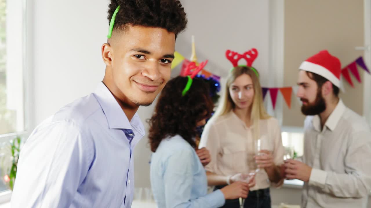 Young office workers talking and holding glasses with sparkling wine during christmas party in the office while their african