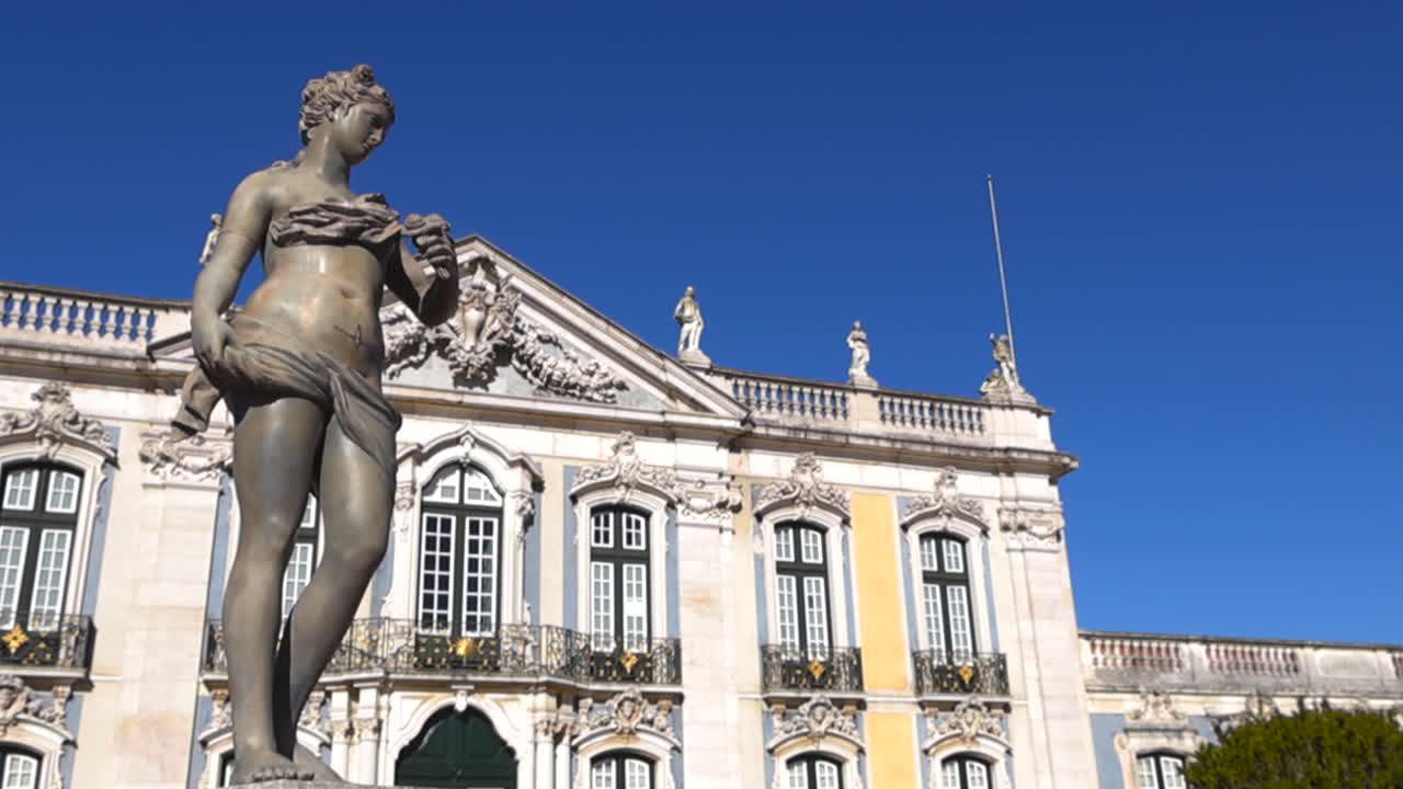 Orbite douce à faible angle autour d’une sculpture classique de femme en marbre dans les jardins du Palais National de Queluz, avec une façade de palais richement décorée et un ciel bleu clair créant une atmosphère historique élégante