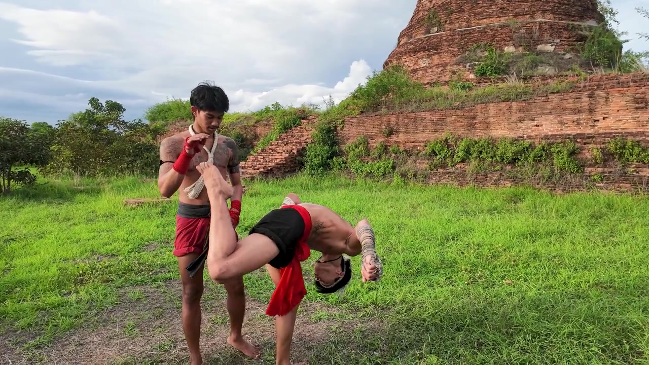 Two Asian fighters practice traditional Muay Thai combat techniques at Ayutthaya Historical Park, Thailand.