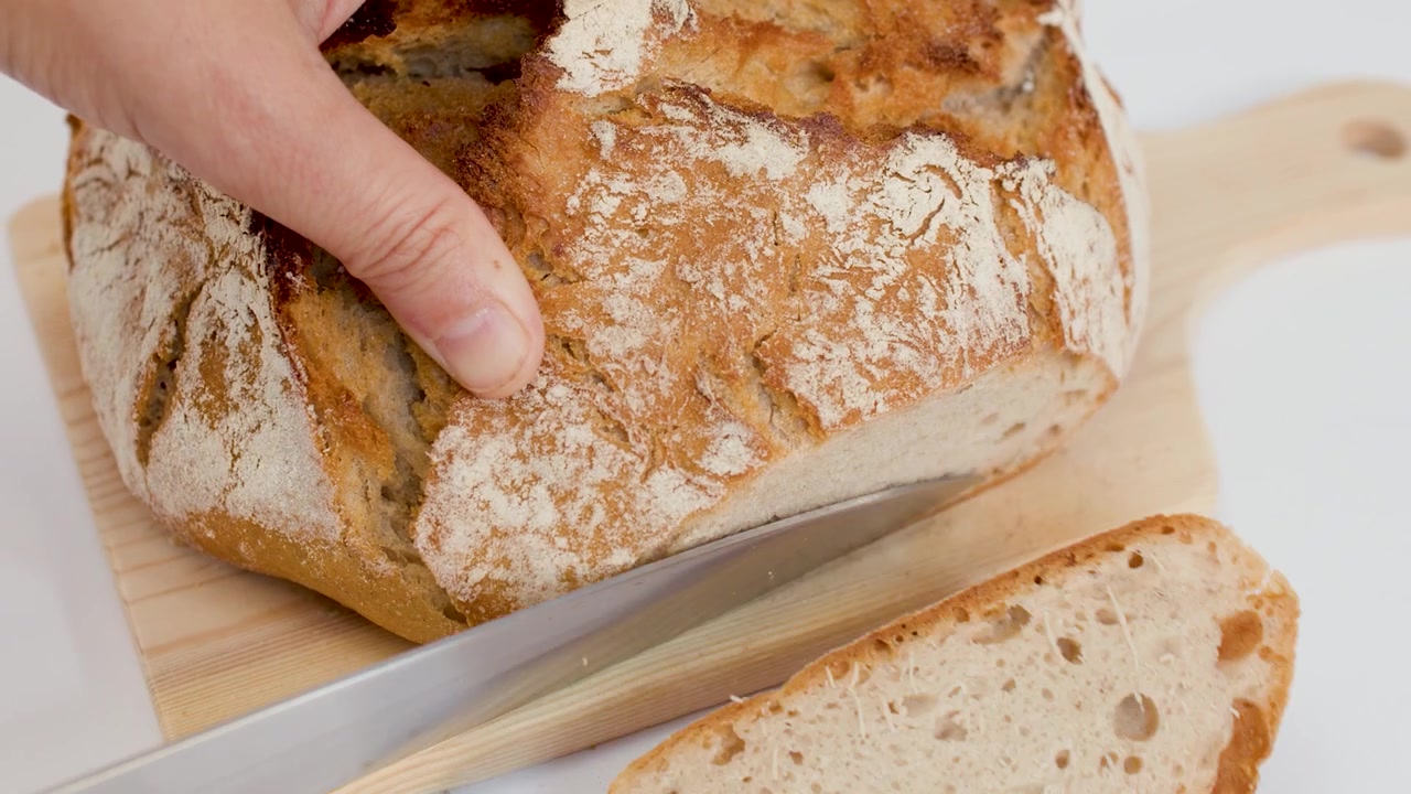 Person Slicing Fresh Crusty Sourdough Bread on Wooden Board