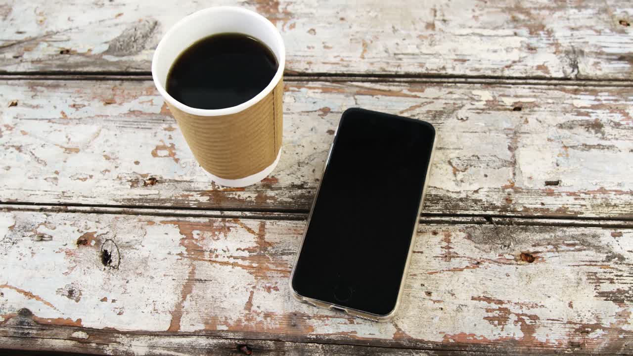 taza de café desechable y teléfono móvil en una tabla de madera