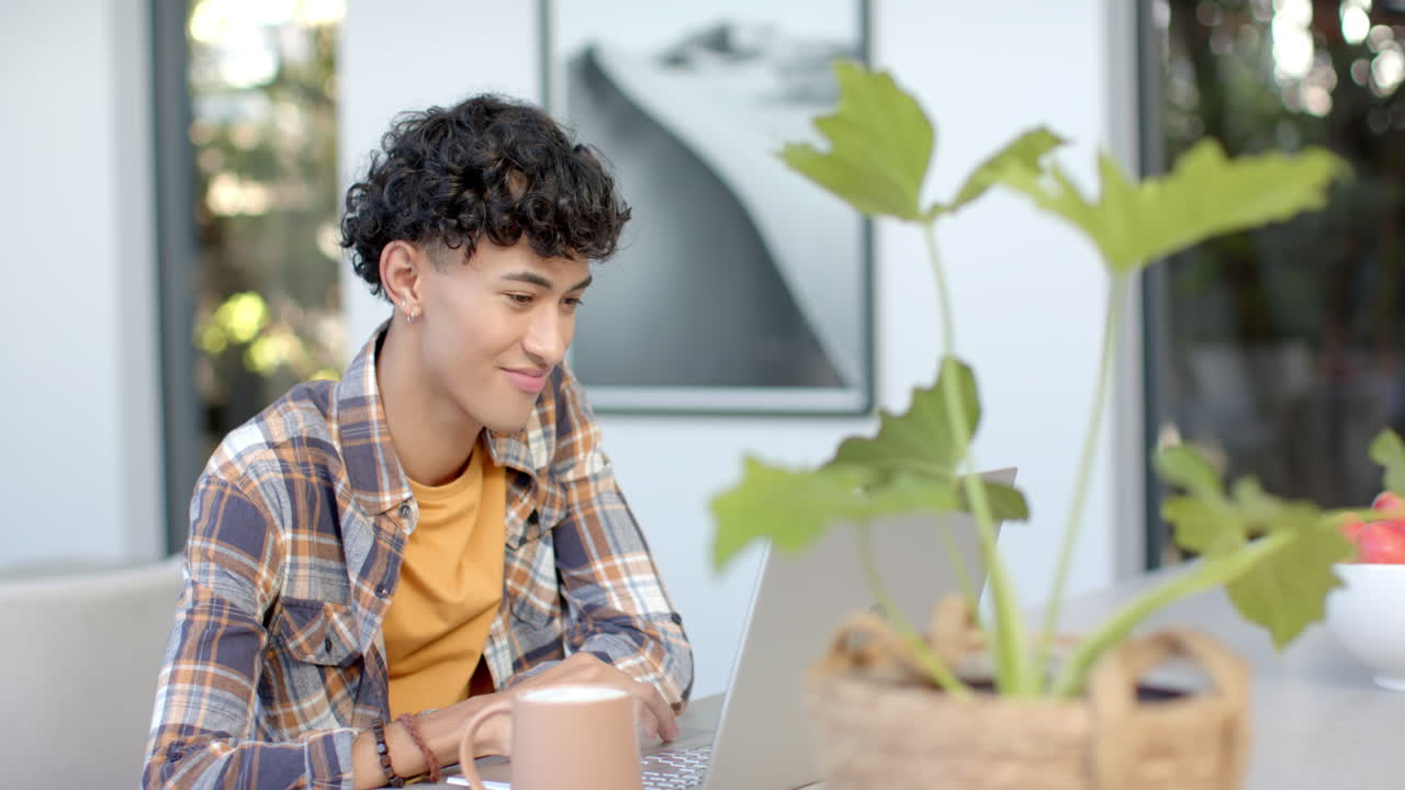 Using laptop and smiling, young man working from home with coffee mug