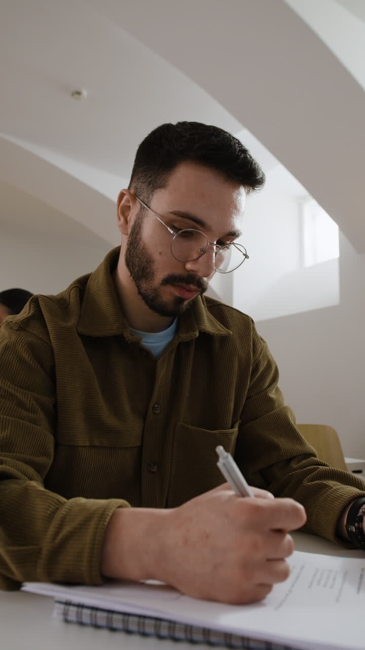 Student writing in a classroom with a professor in the background