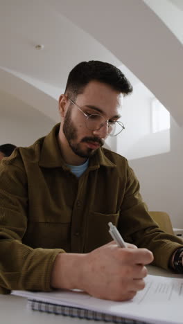 student writing in a classroom with a professor in the background