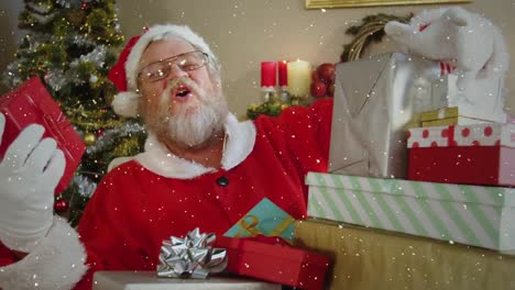 video composition with falling snow over santa  at desk with gifts